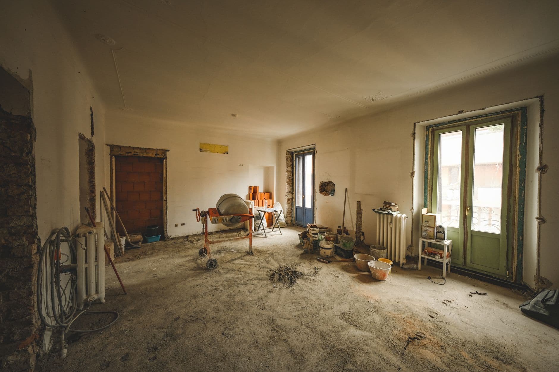 Ruime kamer in renovatie met een kale vloer, een betonmolen, gereedschap en een glazen deur met groen kader