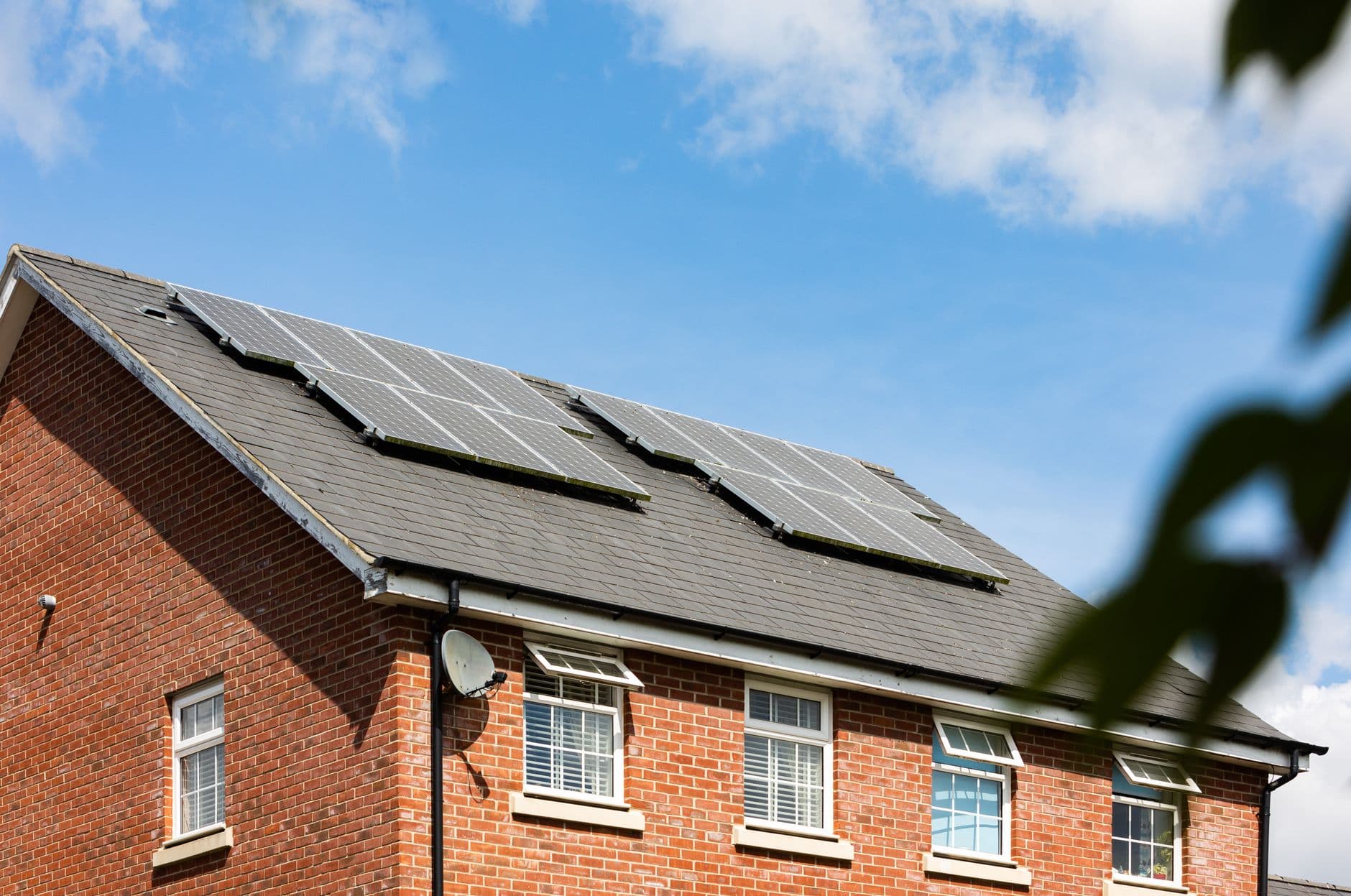 Bakstenen woning met zonnepanelen op een donker dak en witte ramen onder een blauwe lucht