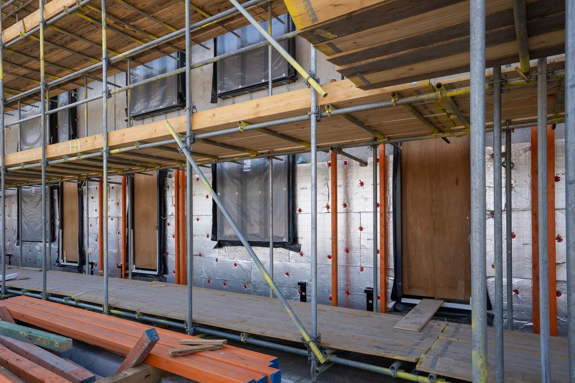 Gevel van een woning achter steigers, bekleed met zilverkleurige isolatieplaten rond de raamopeningen