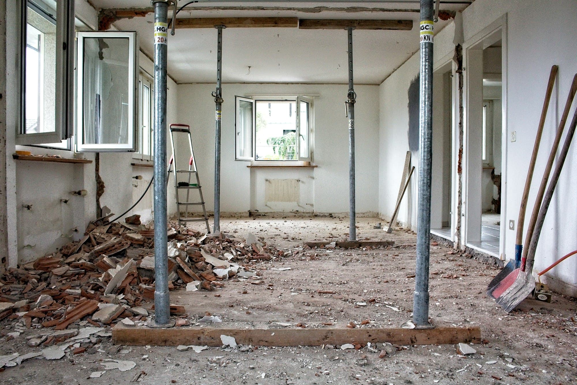 Kamer in renovatie met stalen stempels onder het plafond, puin op de vloer en een open raam