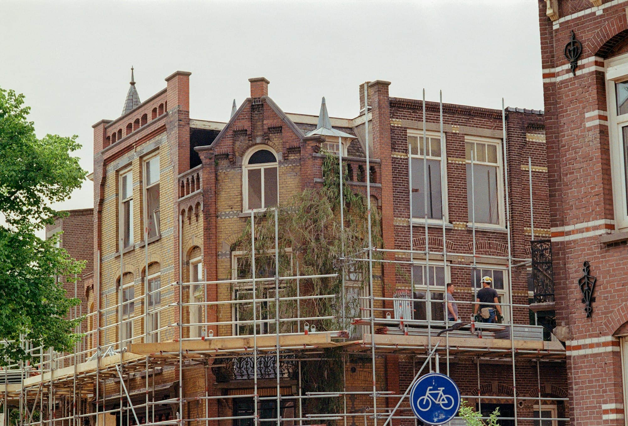 Oud bakstenen gebouw met sierlijke gevel in de stellingen, met een blauw fietsbord op de voorgrond