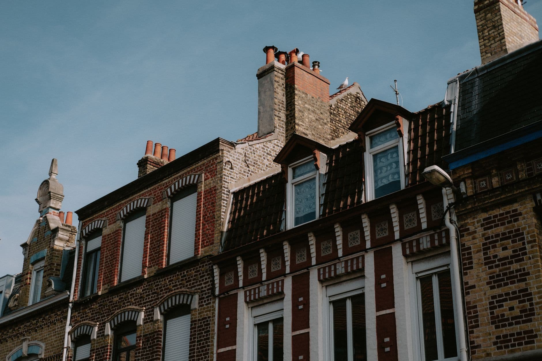 Oude bakstenen rijhuizen met sierlijke gevels, dakkapellen en hoge schouwen onder een blauwe lucht